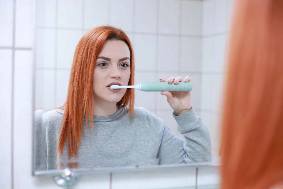 A red-haired girl brushes her teeth.