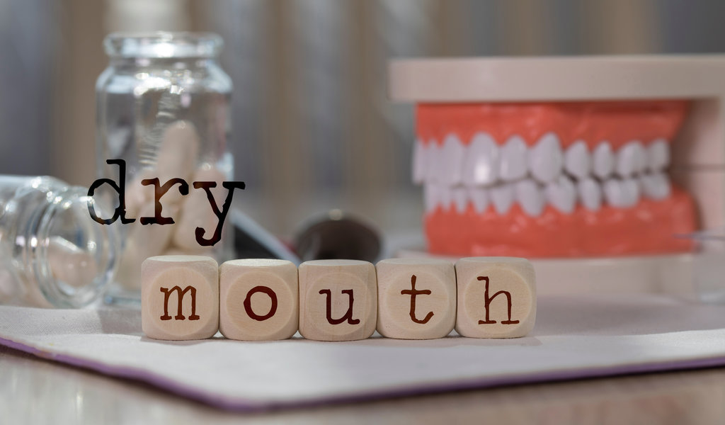 Words DRY MOUTH composed of wooden dices. Pills, documents, pen, human jaw model in the background. Closeup