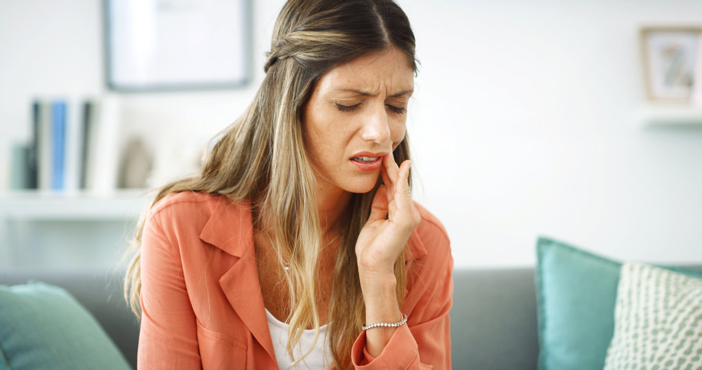 Woman, relax and pain from toothache at house with cavity, dental problem and gum infection. Female person, discomfort and touch cheek for sore gingivitis, root canal injury and tooth decay in lounge.
