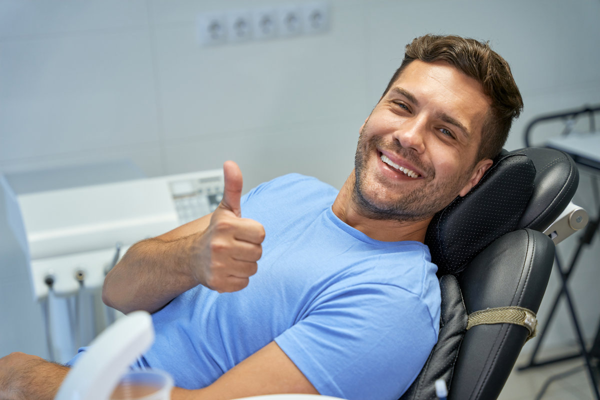 Young brunette man smiling and showing thumbs up while leaning back in a dental chair