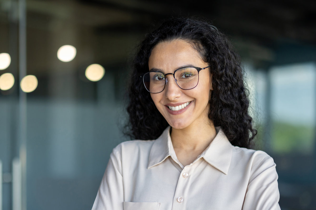Close up photo portrait of beautiful Latin American woman with curly hair and glasses, businesswoman inside office building smiling and looking at camera