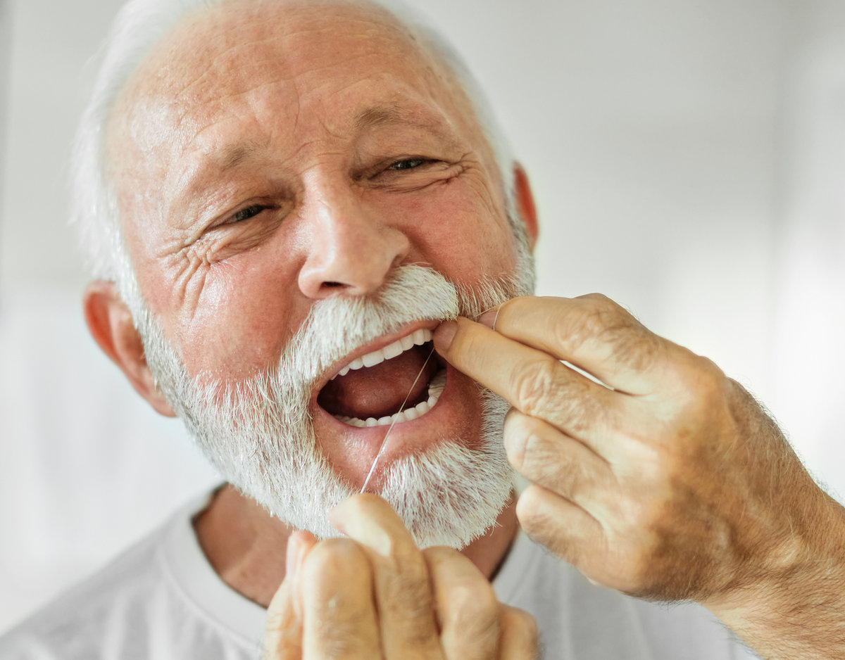 Portrait of an elderly senior man is cleaning brushing his teeth using dental floss in front of mirror in bathroom. Dental hygiene, vitality and beauty concepts